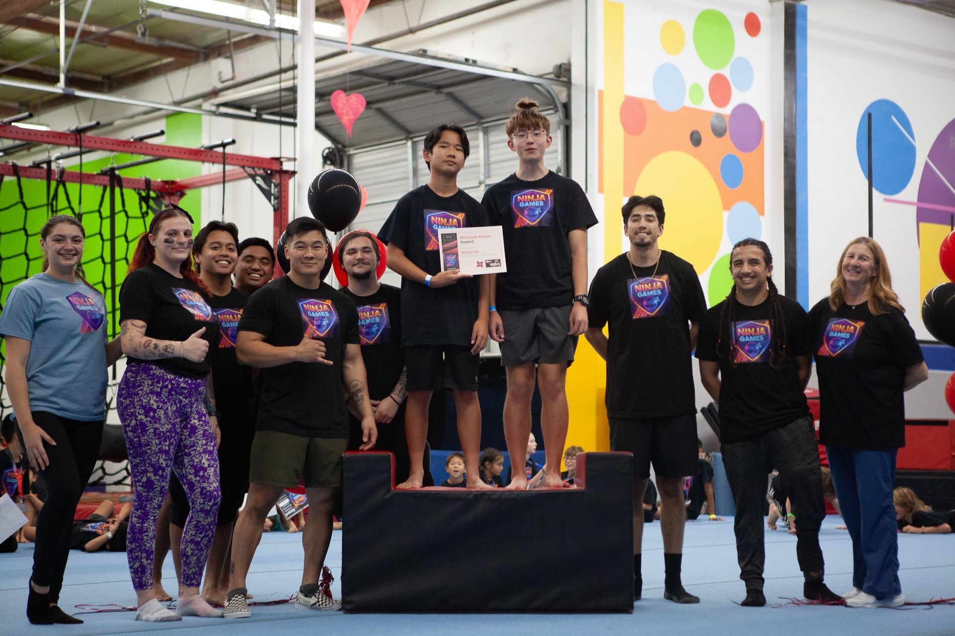 Group posing for photo on a podium inside a gym; award presented to two teens.