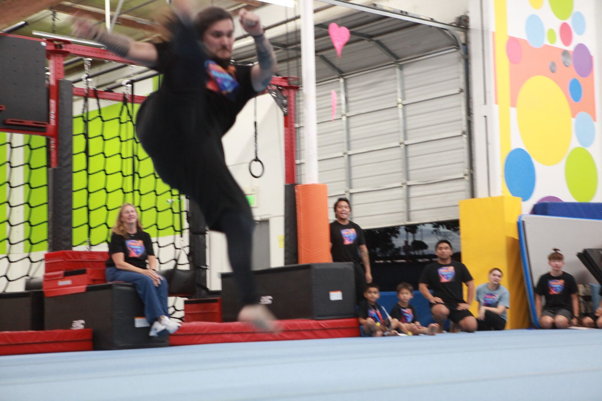 Person leaping during a competition at an indoor obstacle course; spectators watch.