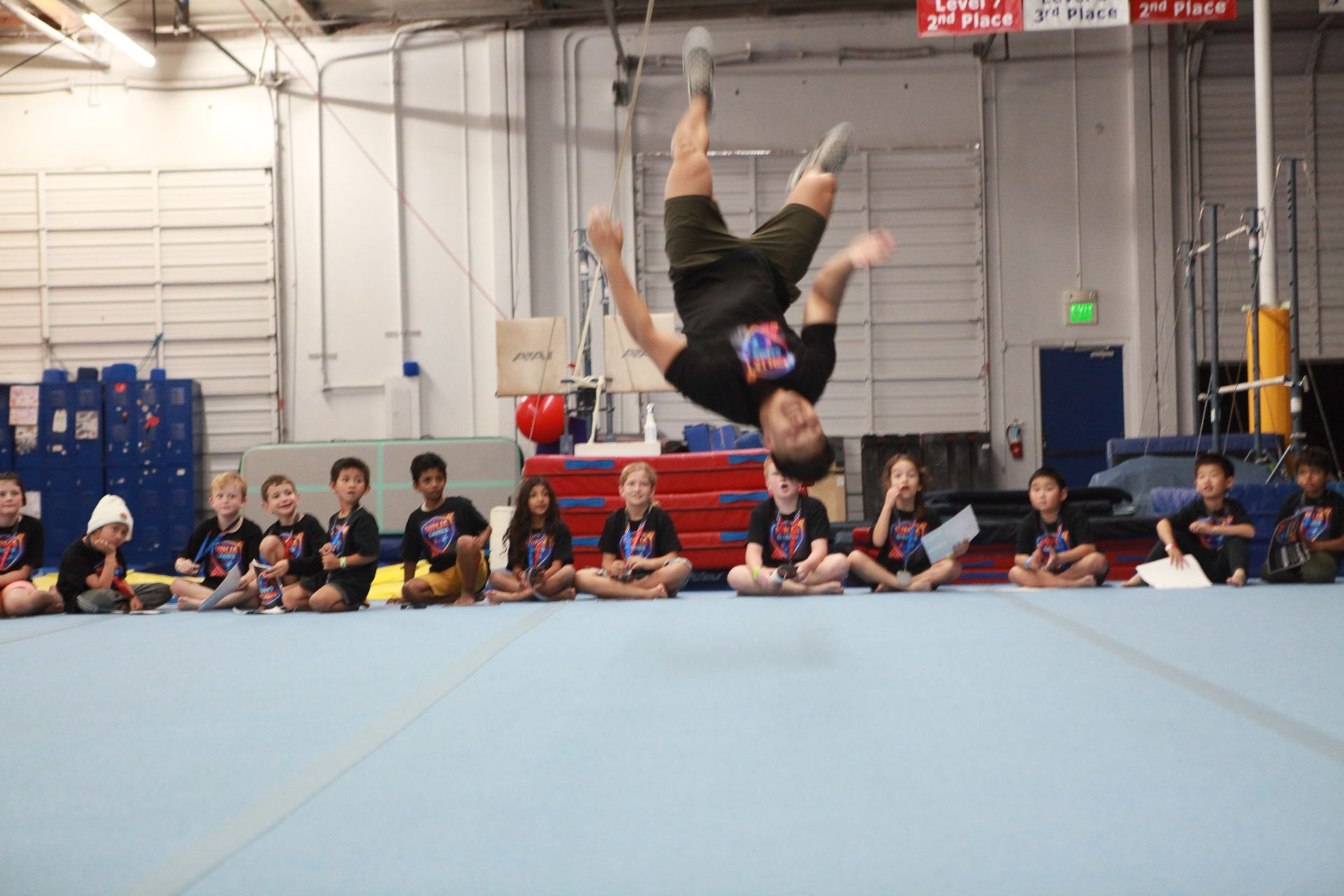 Man doing a backflip in a gym; children watch.