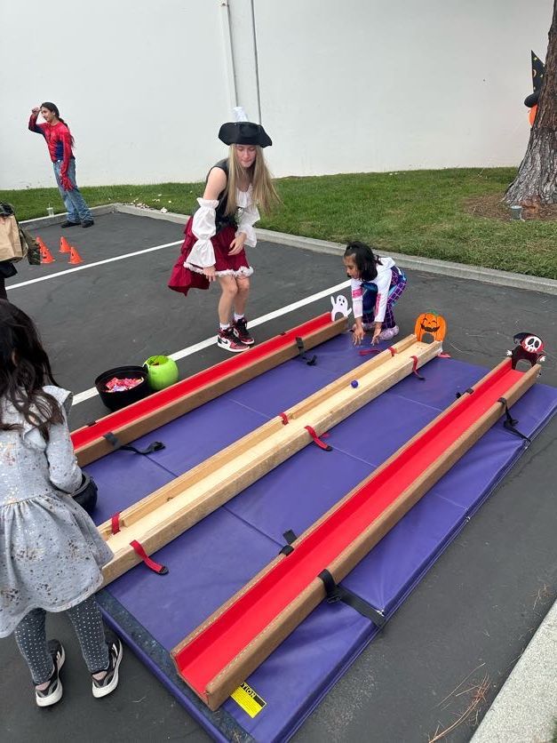 Children playing a marble race game outdoors. One child is dressed as a pirate.