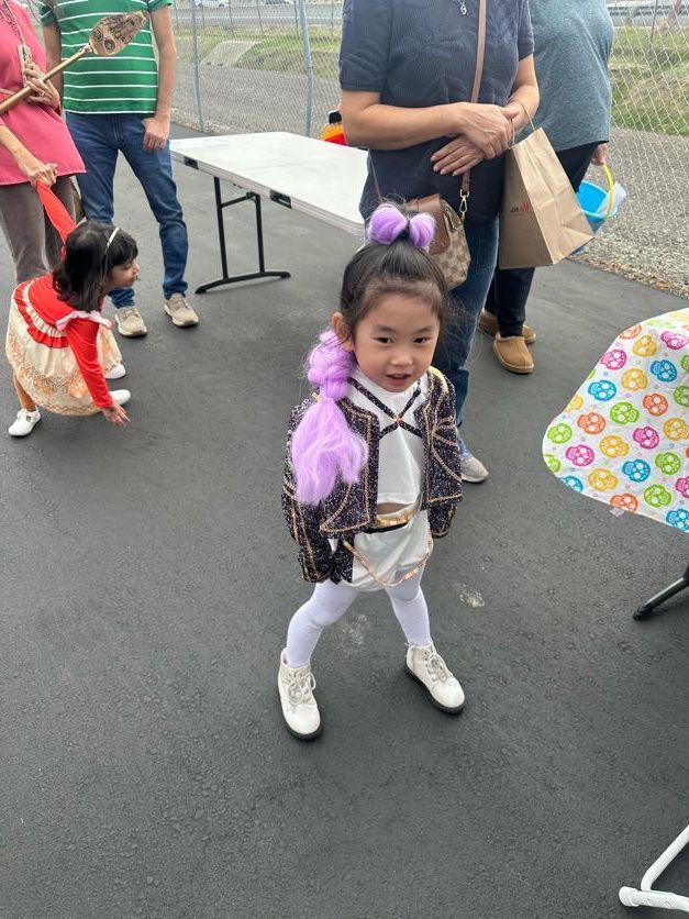 Young child in costume stands on pavement, looking at the camera.