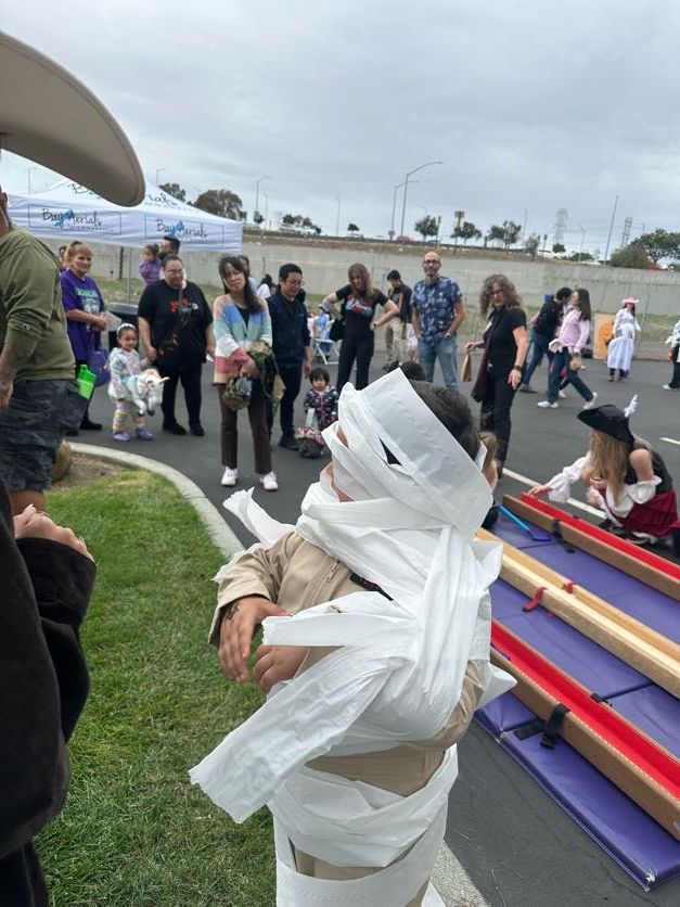 Person wrapped in toilet paper as a mummy at an outdoor event, people in background.