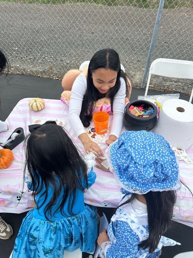 Three children at a table playing games. One girl in a blue bonnet, another in a blue dress, and the third with long hair.