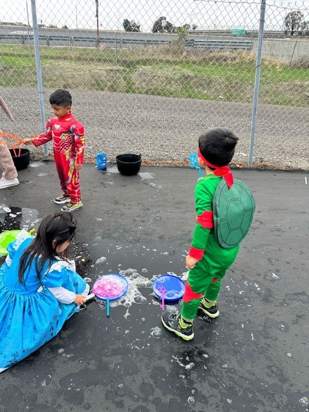 Children in costumes playing with bubbles outdoors.