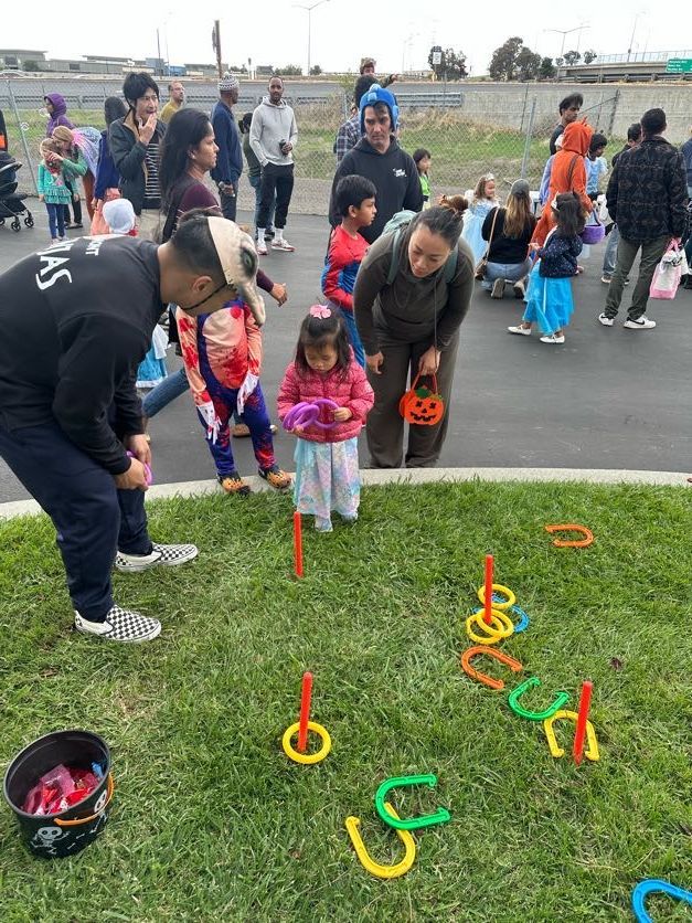 People playing a ring toss game on grass at an outdoor event, with onlookers in the background.