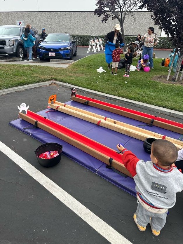 A young child reaches toward a Halloween game. Three wooden tracks with red trim sit on a purple mat.