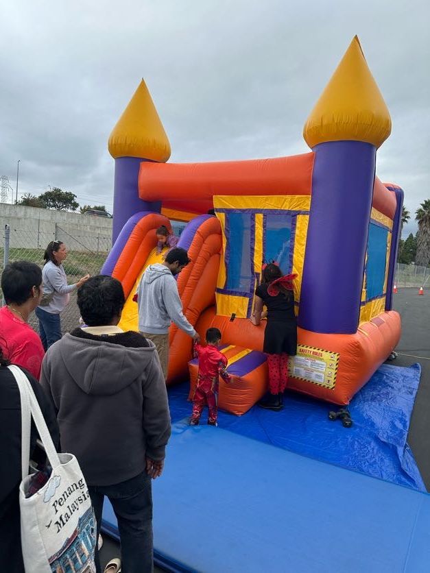 People near a colorful inflatable castle with a slide on a cloudy day.
