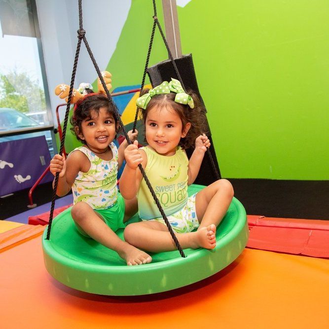 Two little girls are sitting on a green circle swing