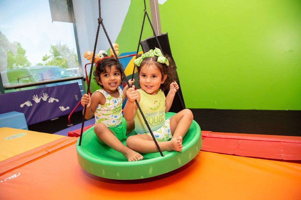 Two little girls are sitting on a swing in a gym.