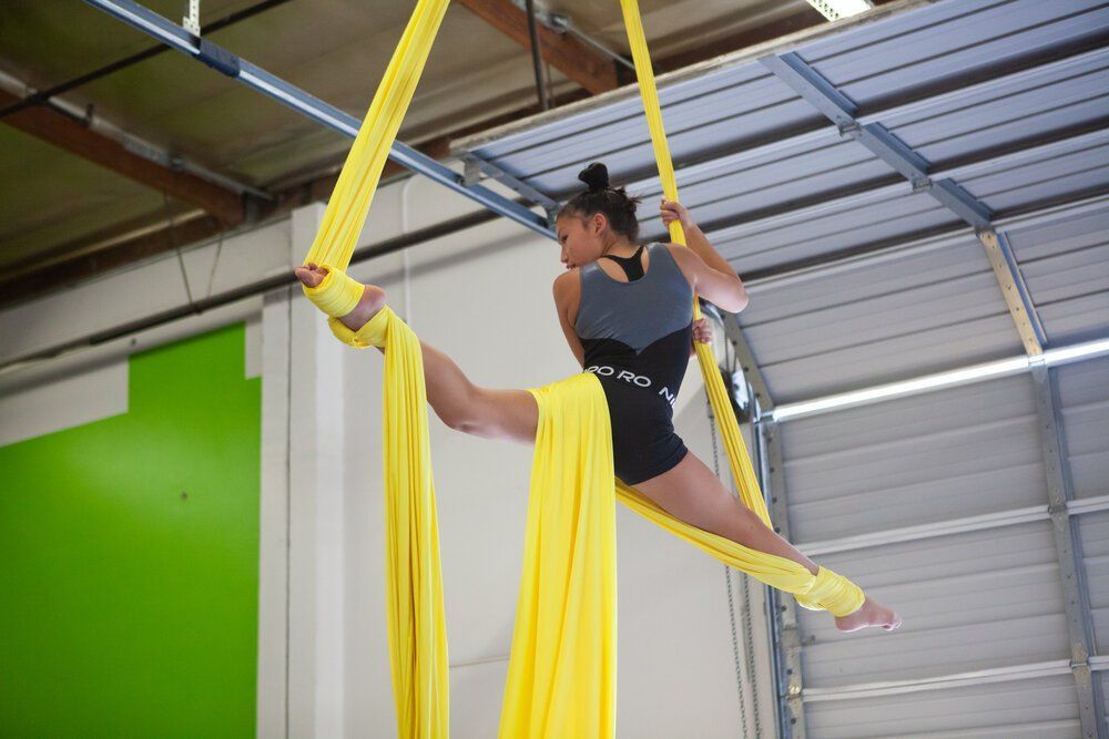A woman is doing aerial silks in a gym.