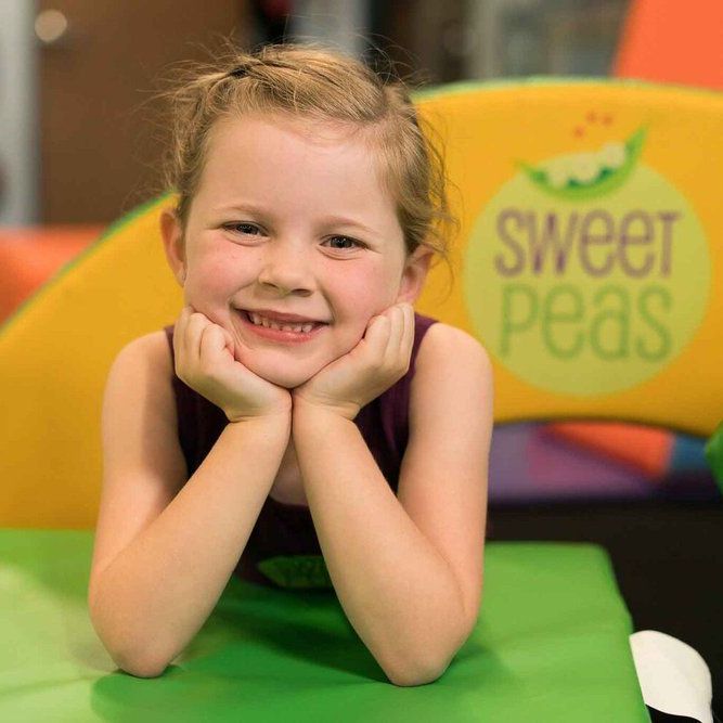 A little girl is smiling in front of a sweet peas sign