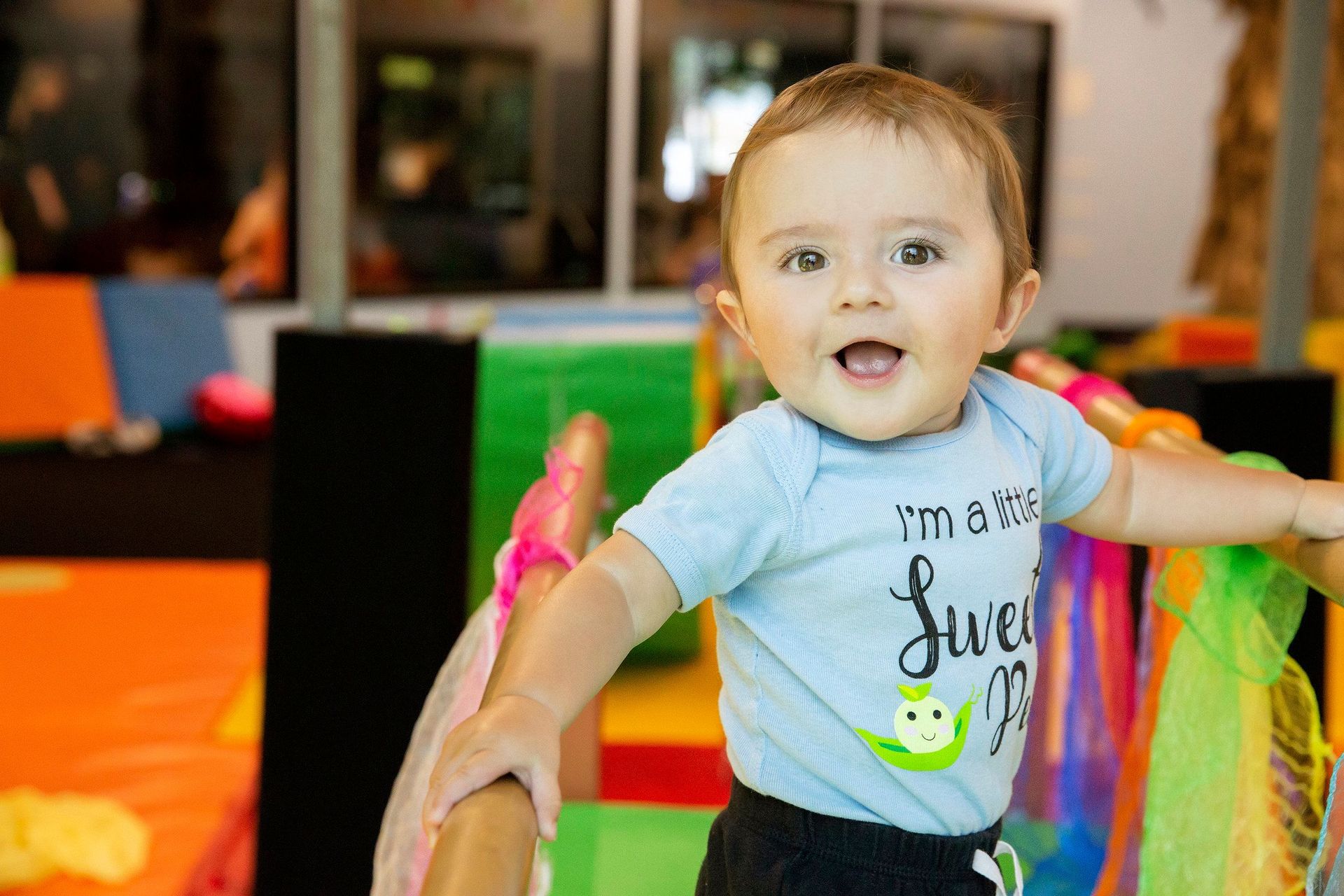A baby in a blue shirt is standing in a playground.