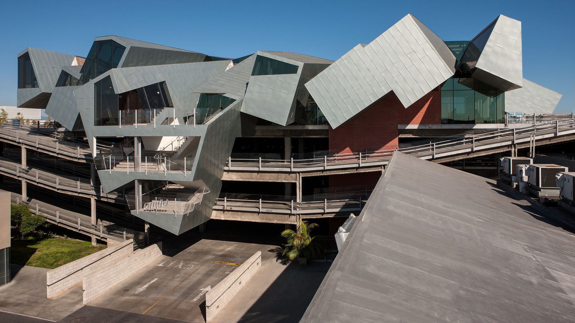 Modern angular building with geometric metal panels and concrete walkways under a blue sky