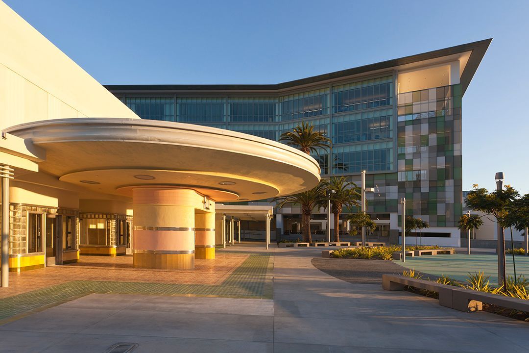 Modern building entrance with a curved canopy, glass facade, and landscaped walkway at sunset