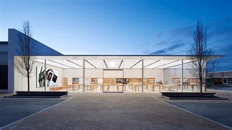A modern Apple Store with a glass facade and flat roof, illuminated from within during twilight.