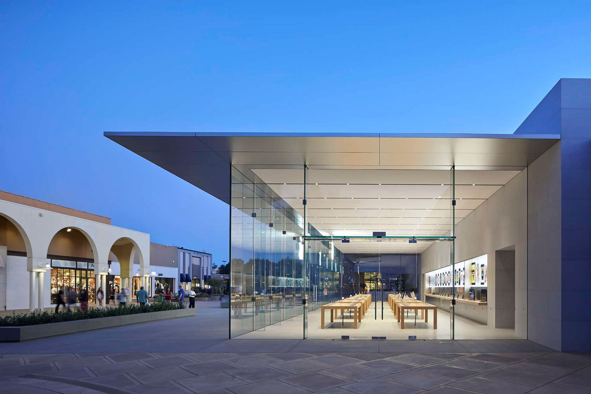 An Apple Store at dusk, featuring a modern glass facade with a minimalist interior and a wide, overhanging roof.