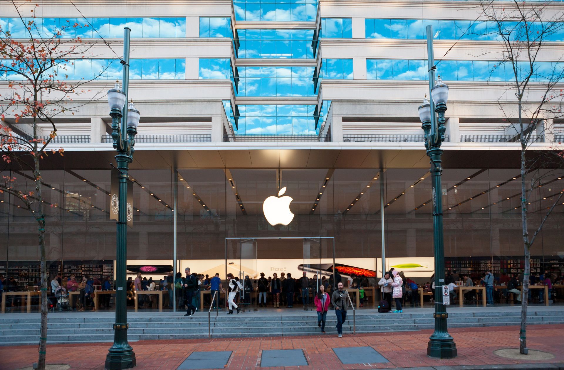 An Apple Store at street level beneath a building, featuring a prominent glowing logo and people walking in front.