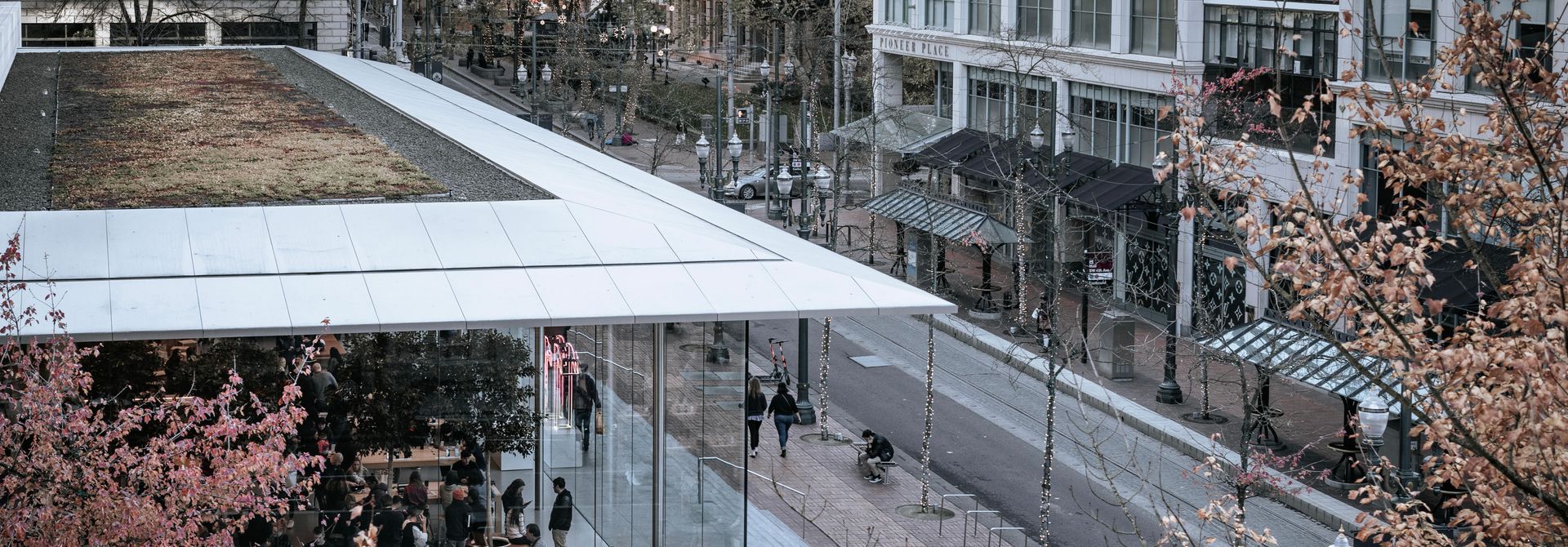 Elevated view of a modern building with a flat roof and glass facade next to a city street with pedestrians.