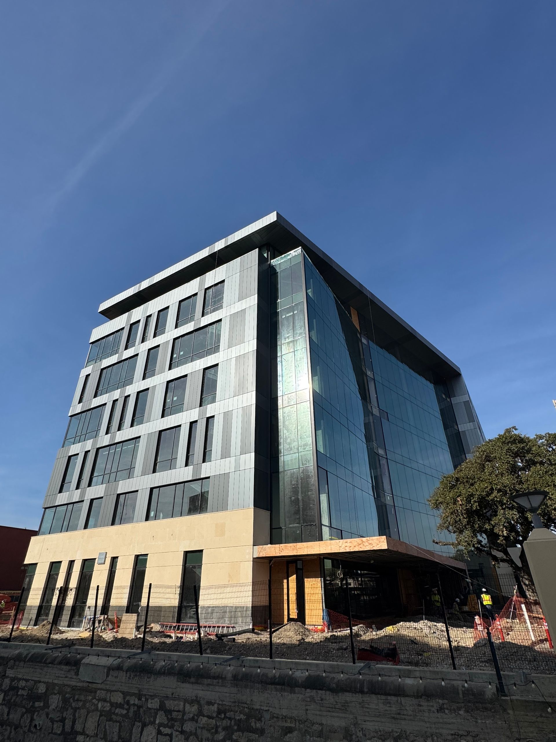 A modern multi-story office building with a glass facade and beige masonry base under a clear blue sky.
