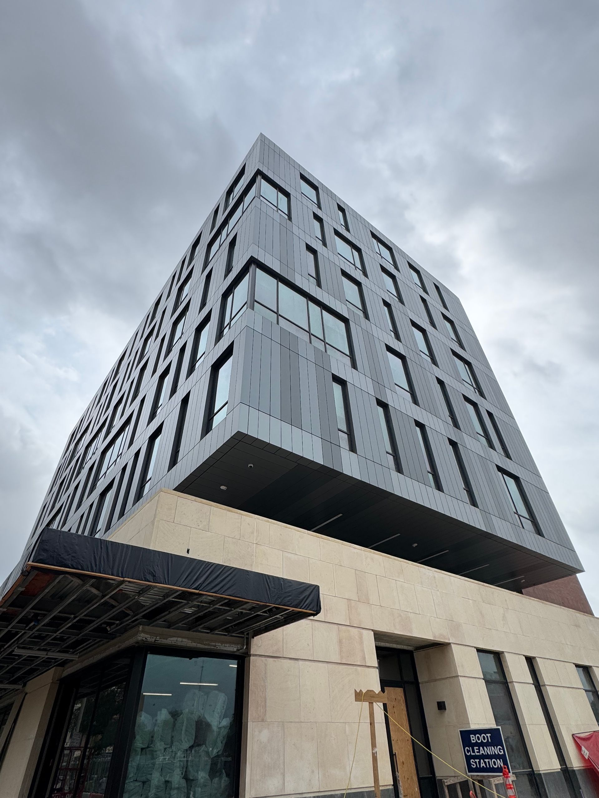 Modern gray-and-beige high-rise building shot from a low angle under a cloudy sky