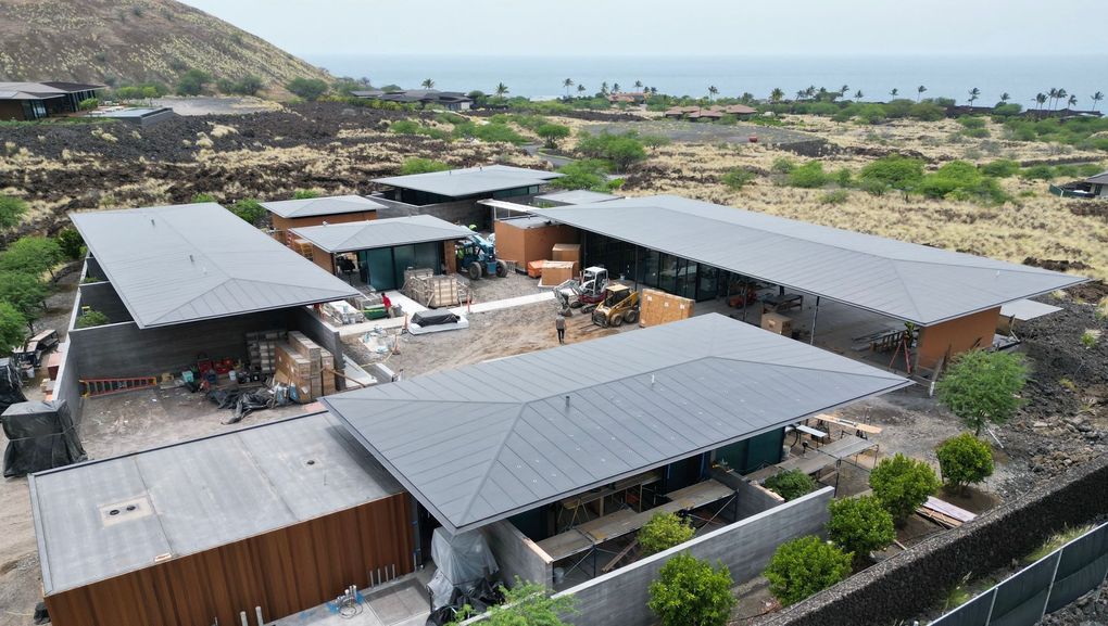 Aerial view of a modern coastal resort with gray roofs, courtyards, and ocean in the distance