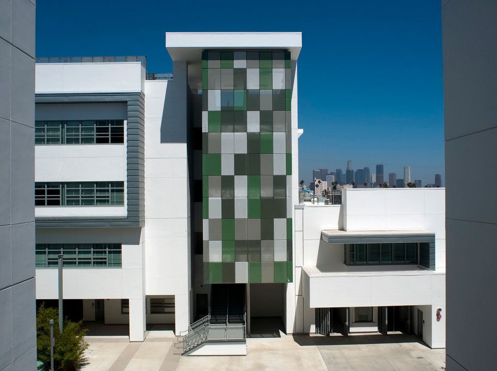 Modern building with green glass facade between white buildings, city skyline in the background