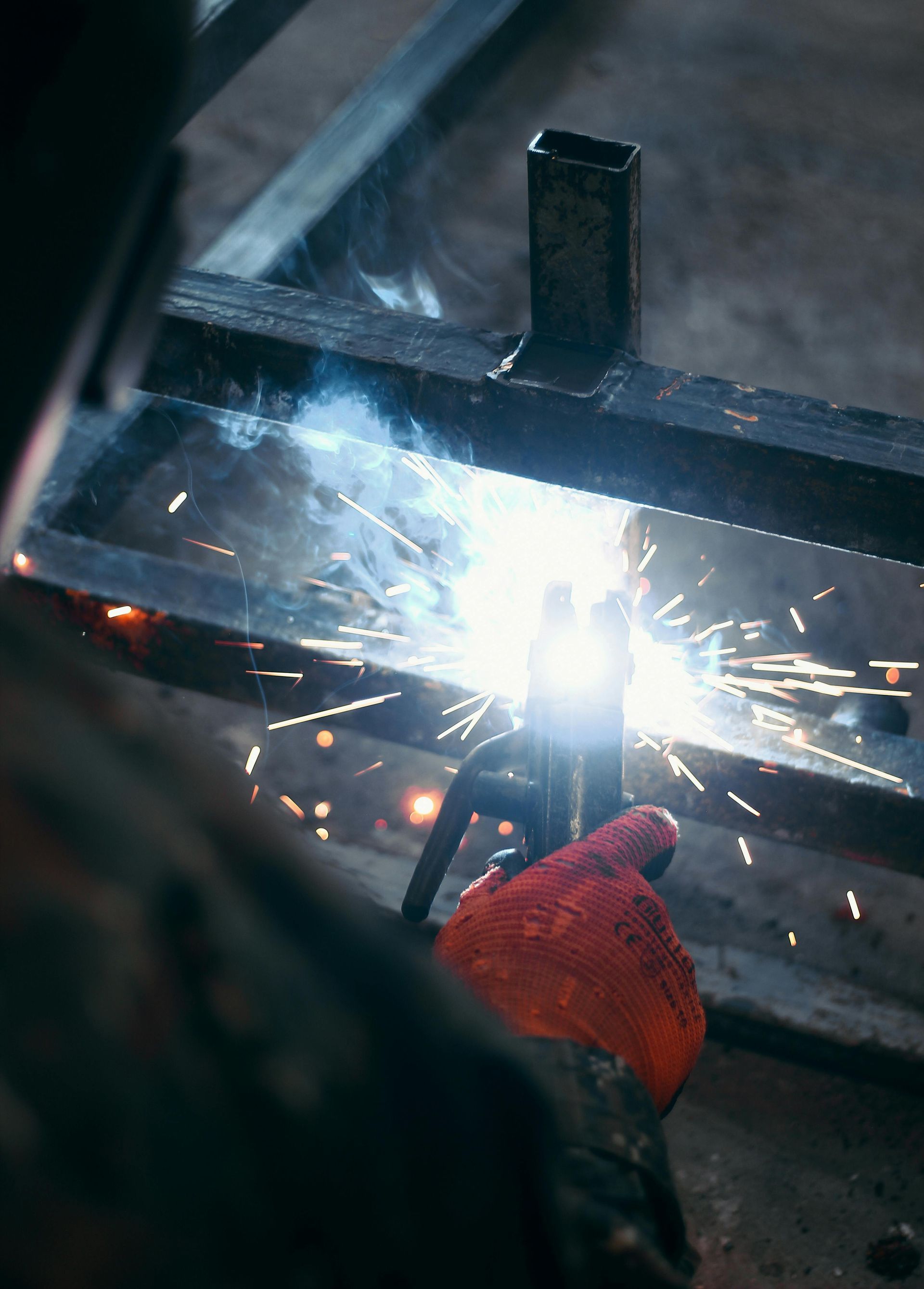Person welding metal with bright sparks in a workshop, wearing an orange glove