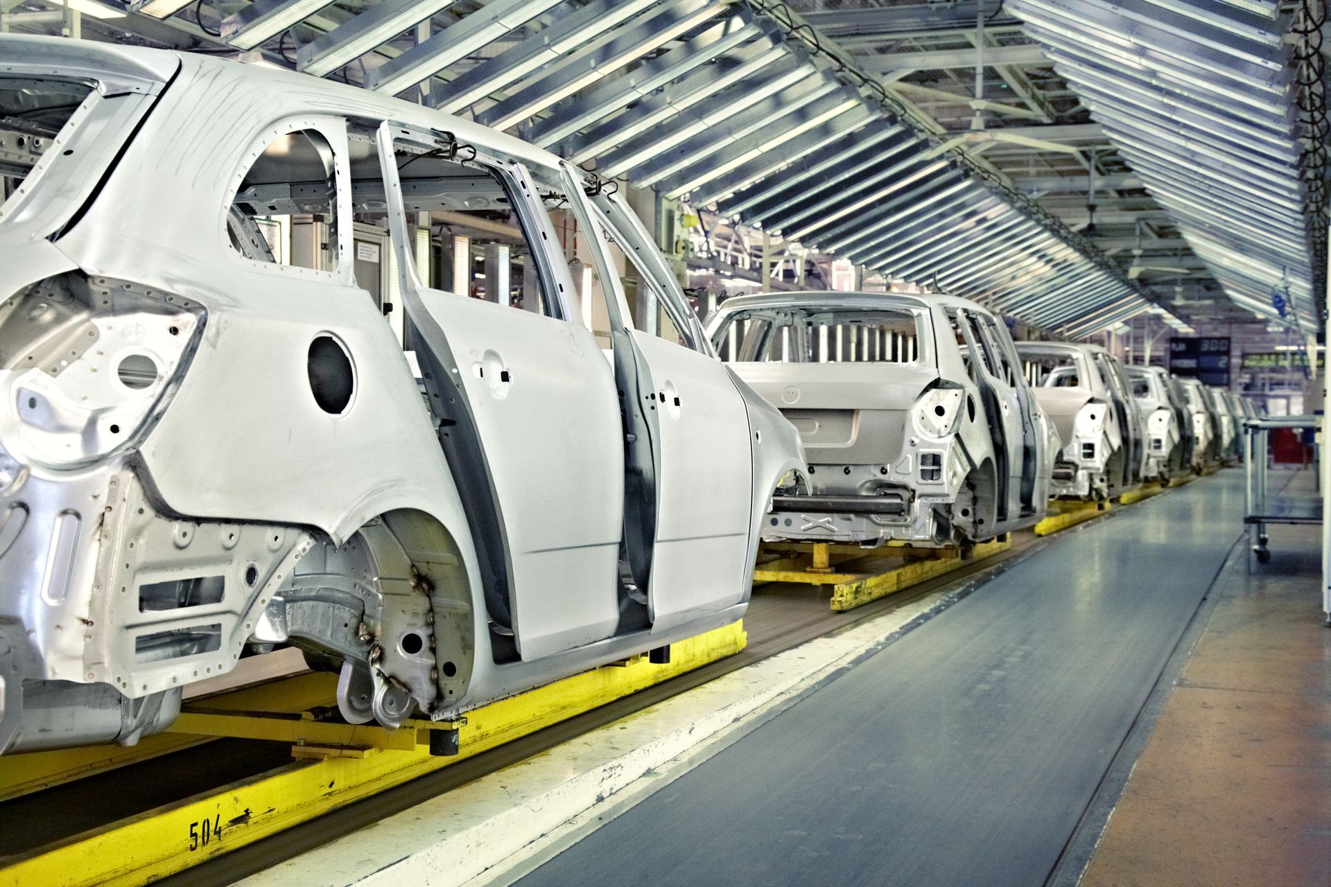 Automobile factory assembly line with white car bodies moving along a bright production floor