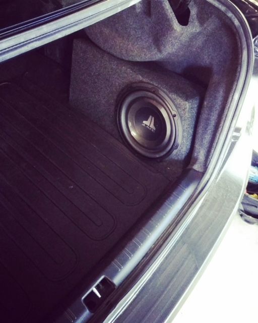 Car trunk lined with a custom black subwoofer enclosure and speaker