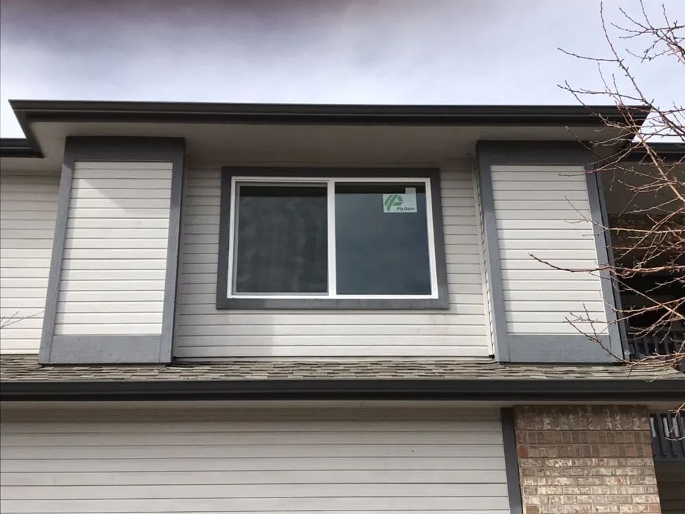 Exterior of a building with a window, white siding, and gray trim under a cloudy sky.
