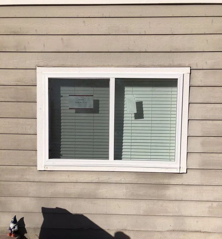 Window with white frame on a light brown wood-paneled wall, blinds visible.