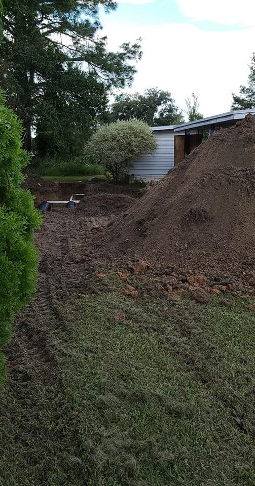 Pile of dirt next to a small building. Grass in foreground, trees in background. Cloudy sky.