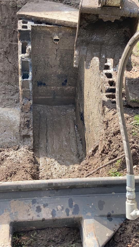 Excavated trench exposing a concrete structure, possibly for utility work, with a backhoe visible.