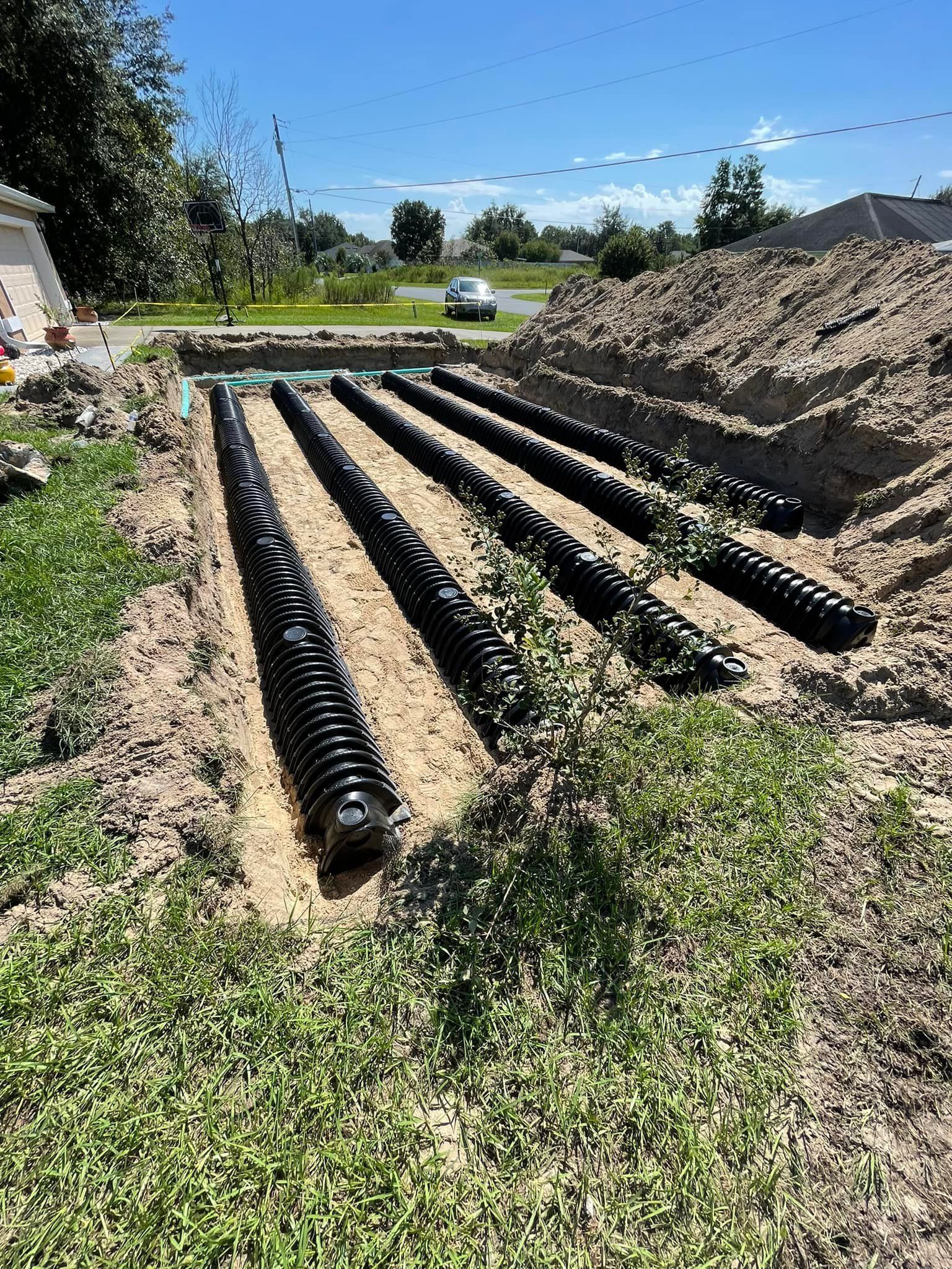 Black drainage pipes in trenches, in a yard; under blue sky.