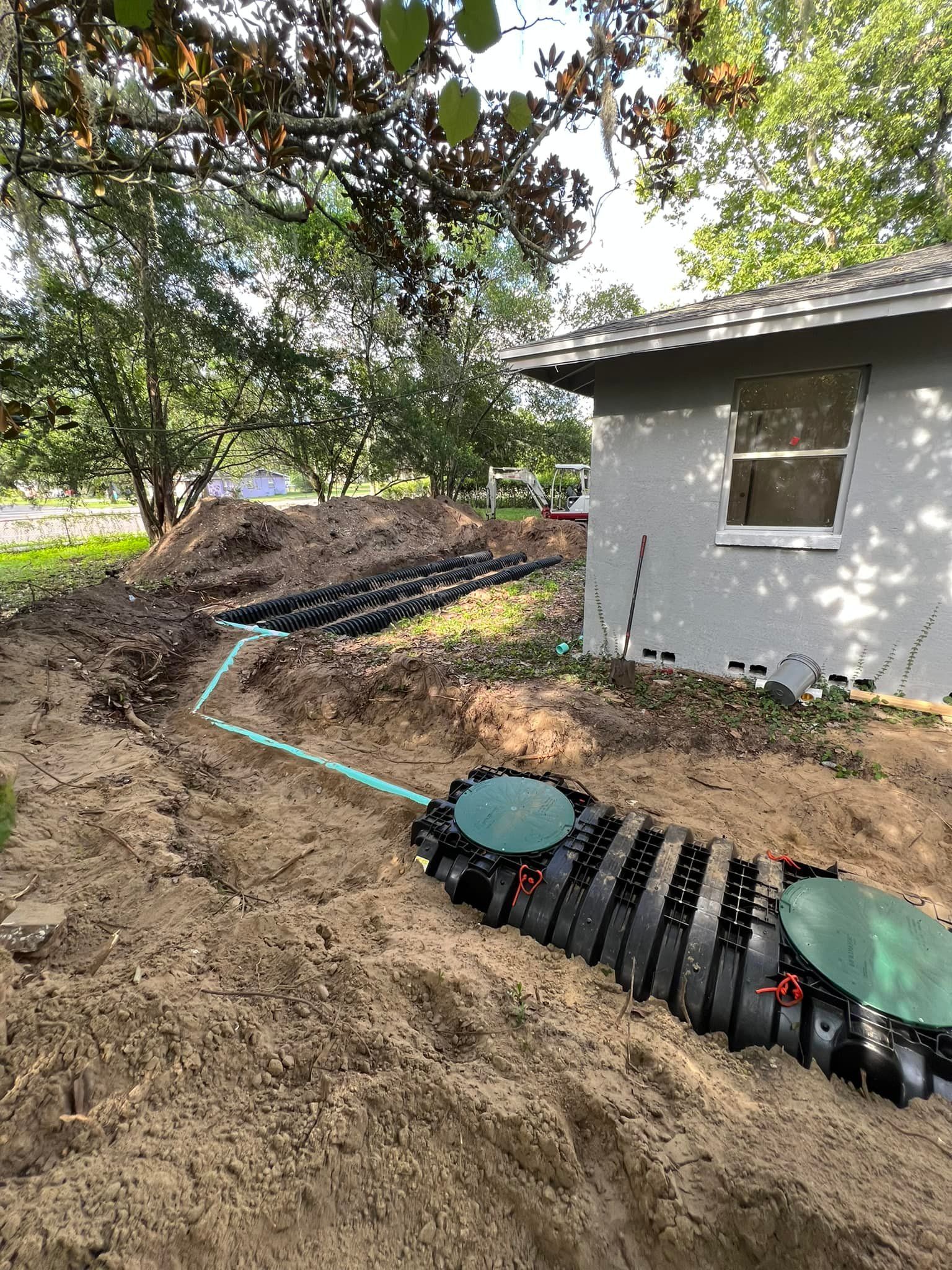 Septic system installation near a house; pipes, tanks, and soil visible in an outdoor setting.
