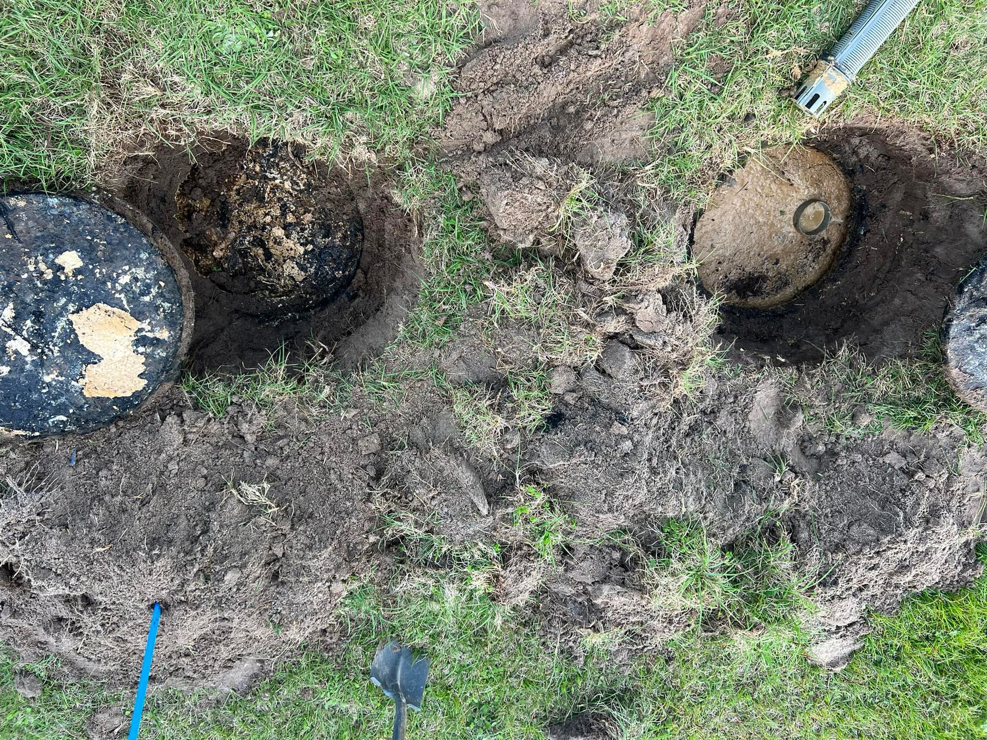 Three circular access points dug up in grass, dirt pile in between.