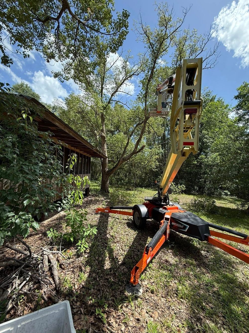 A tree trimming lift truck in use next to a house under a tree.