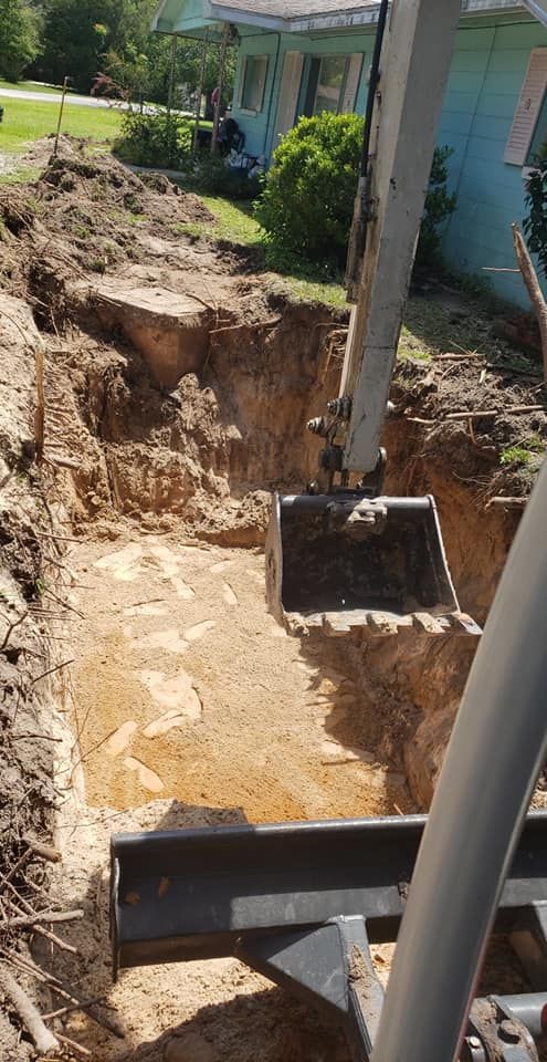 An excavator digging a rectangular trench in a yard, near a house with a green lawn.