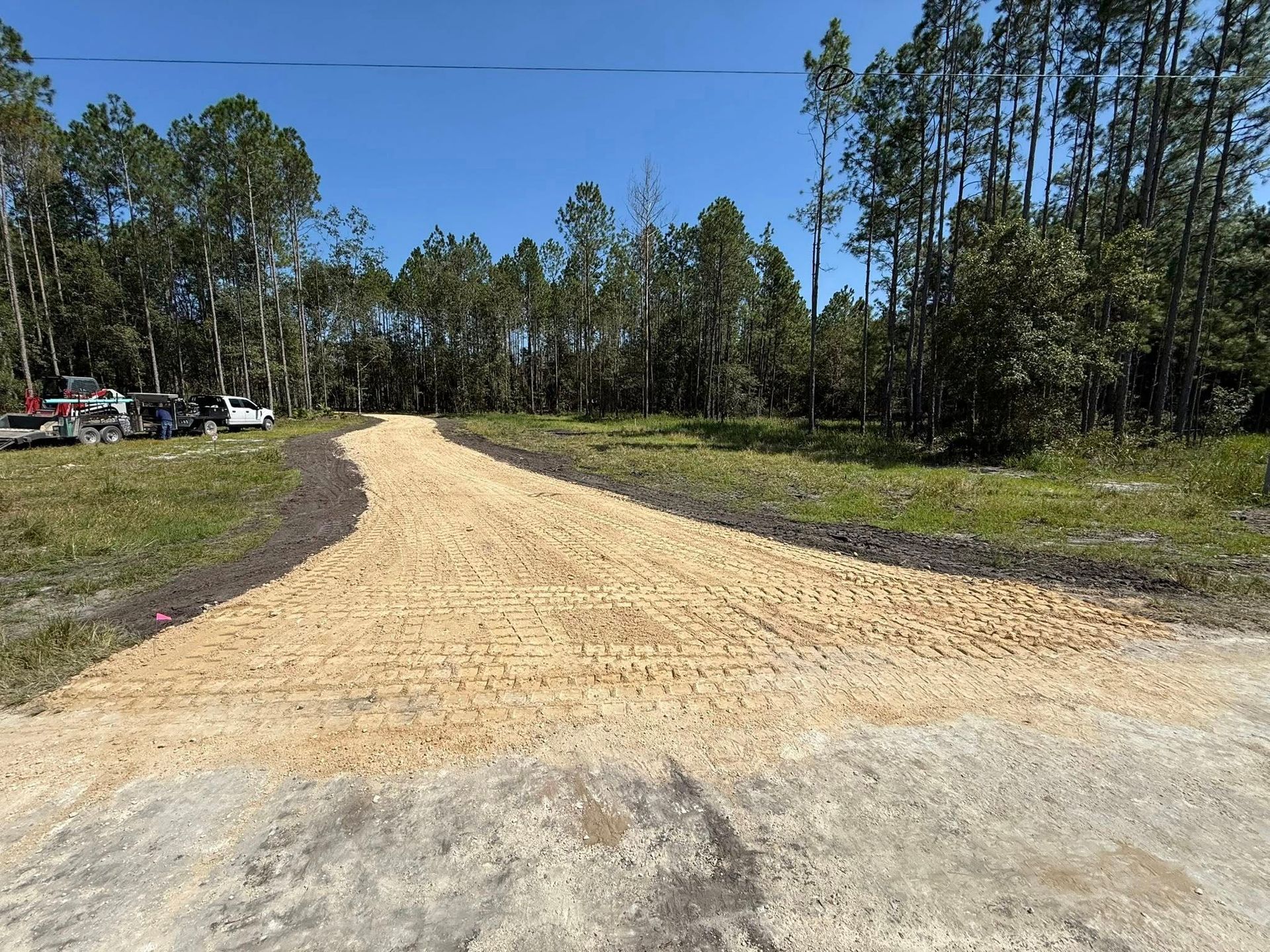 Gravel path between a white fence and a gray building under a cloudy blue sky.