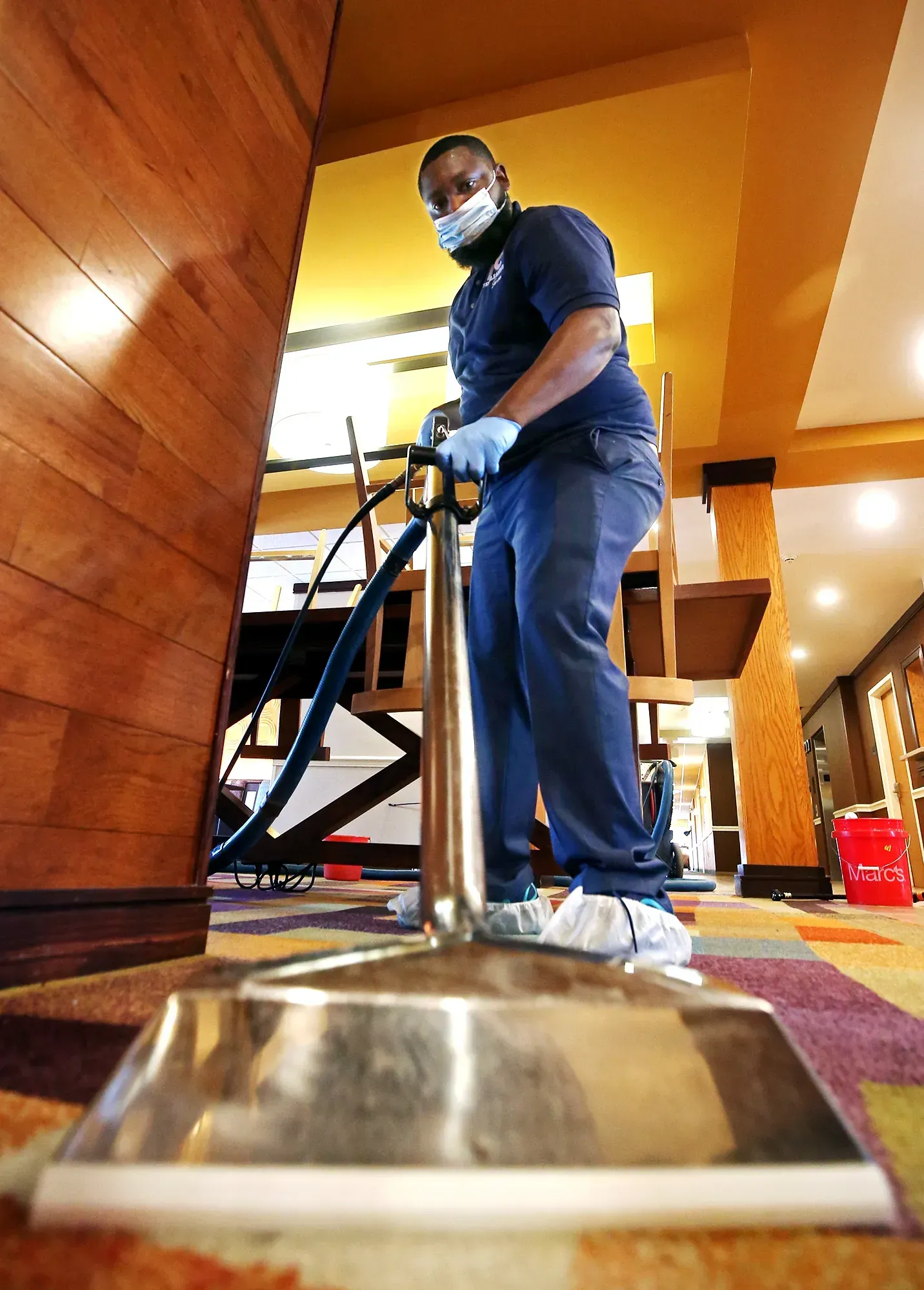 Person holding cleaning supplies, another mopping floor, in a well-lit room.