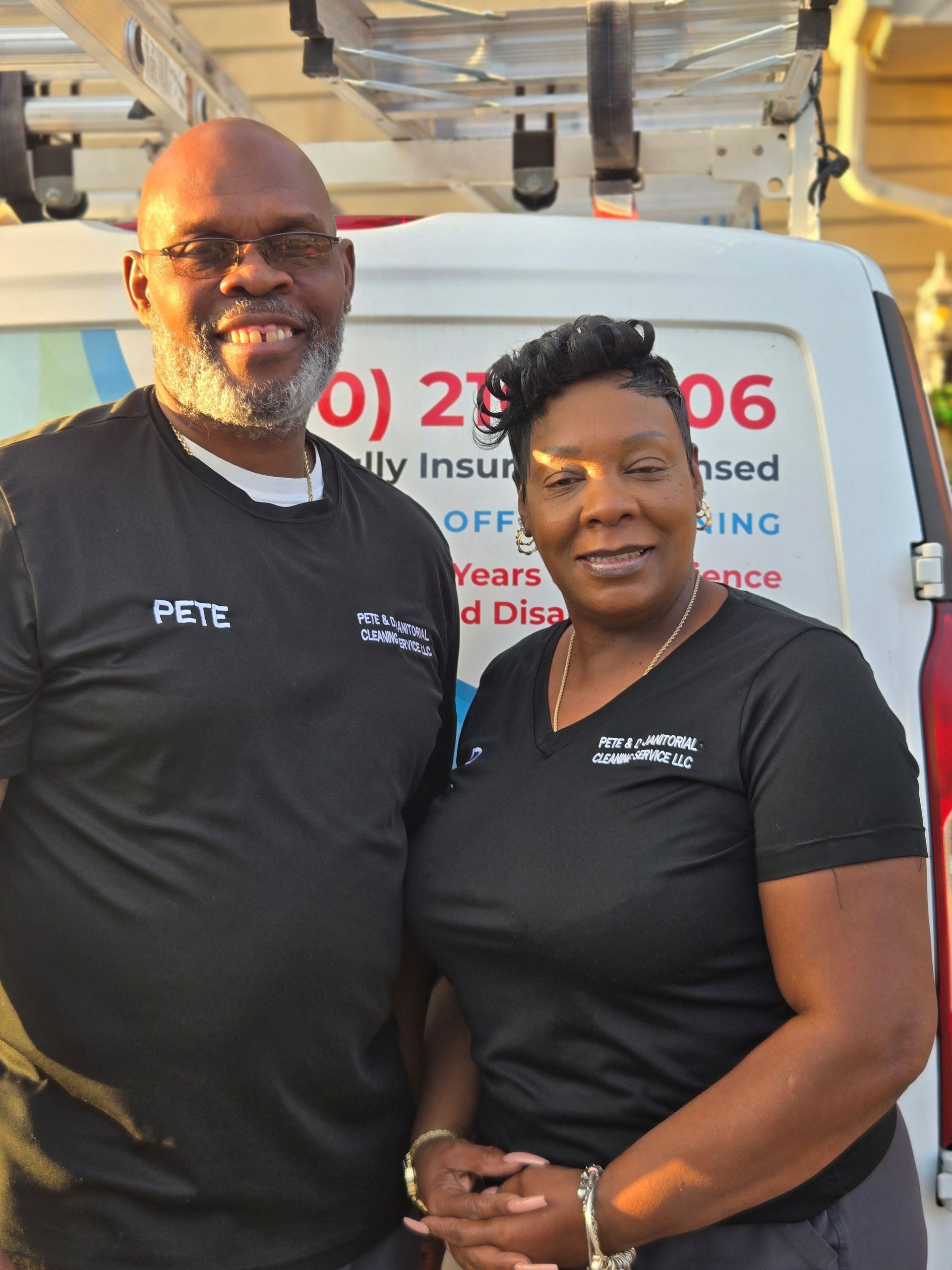 Two people stand in front of a white van with business information. Man wears glasses and a shirt that reads Two people stand in front of a white van with business information. Man wears glasses and a shirt that reads