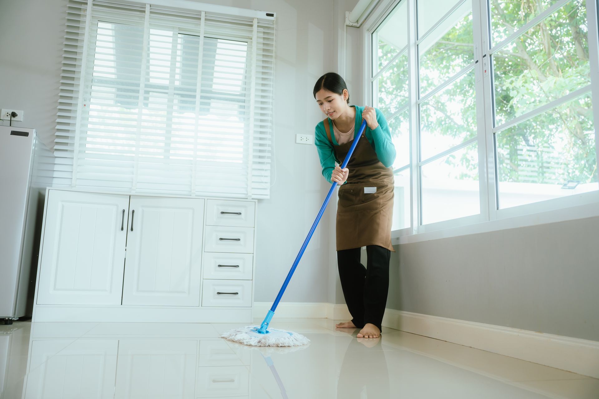 Person mopping a bright room with large windows and white cabinets