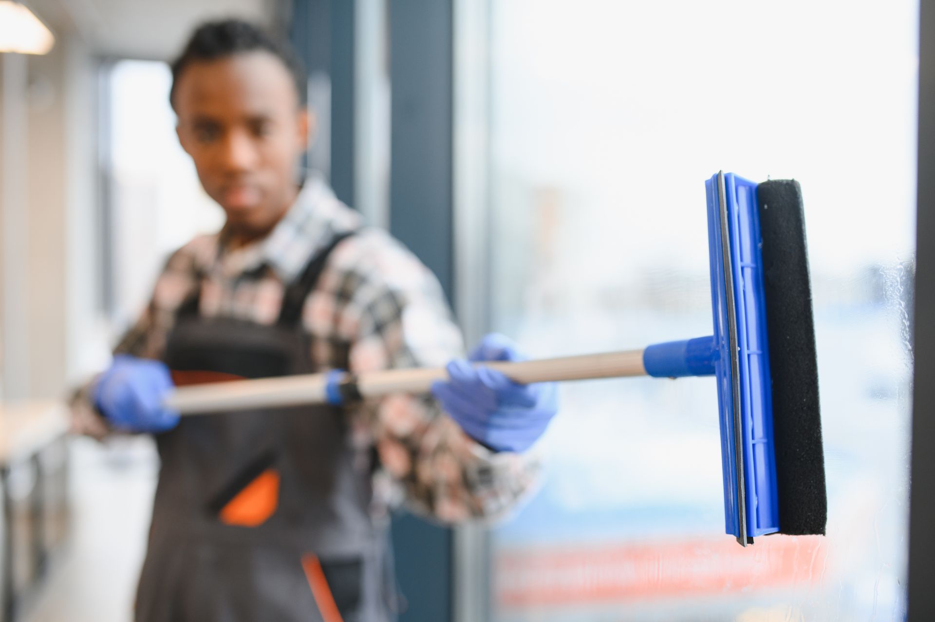 Man in overalls and gloves cleaning a window with a squeegee.