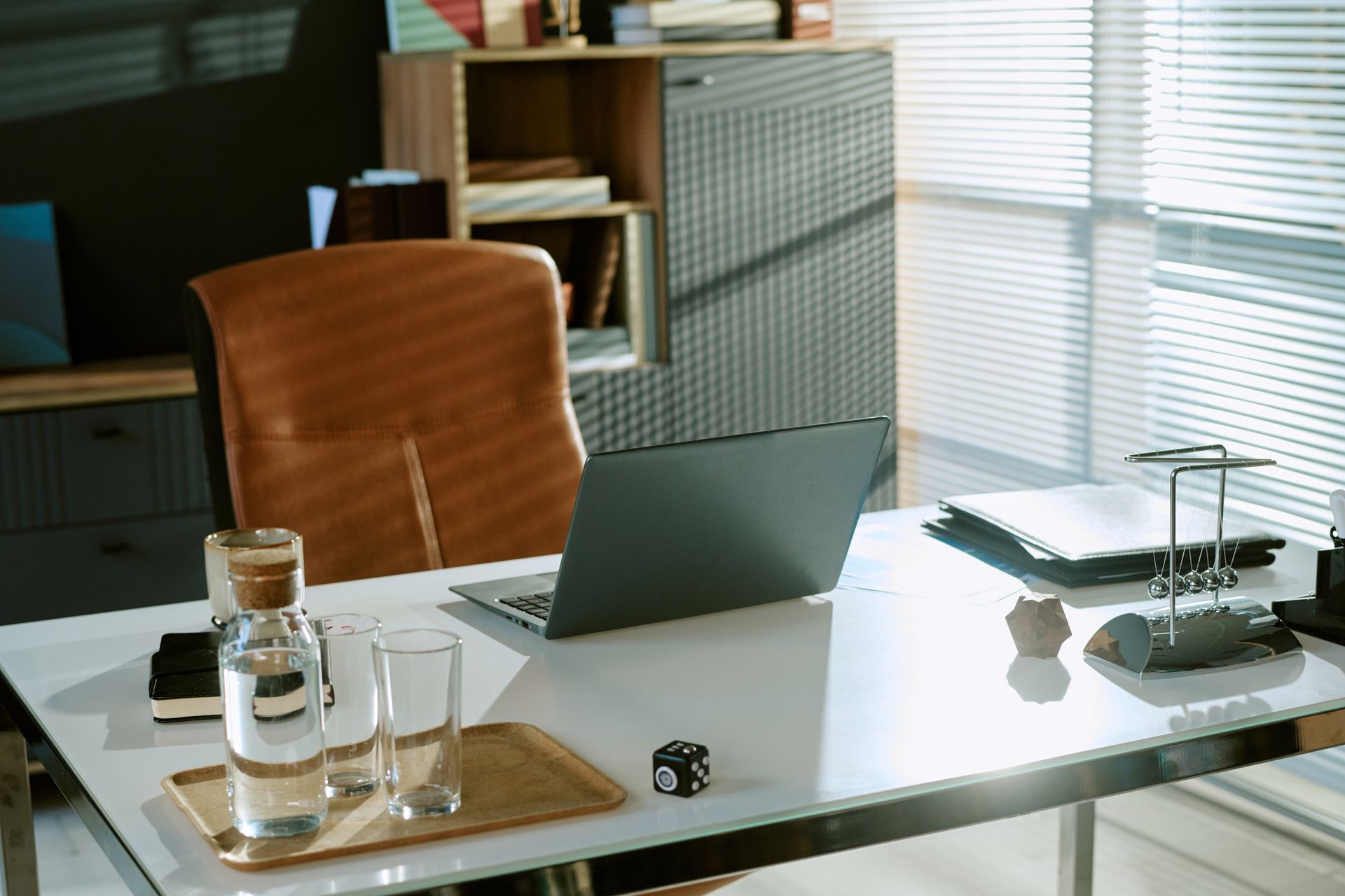 Modern office desk with open laptop, water bottle, glasses, chair, asnd window blinds