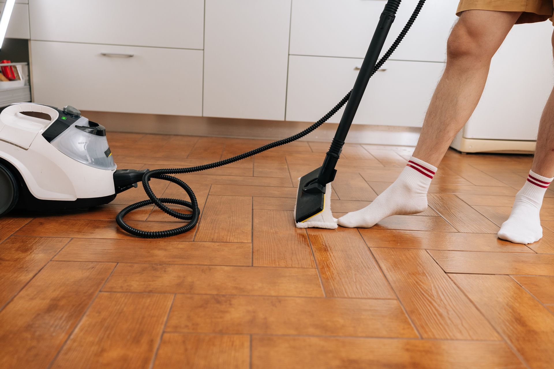 Person mopping a wooden kitchen floor with a white steam cleaner nearby