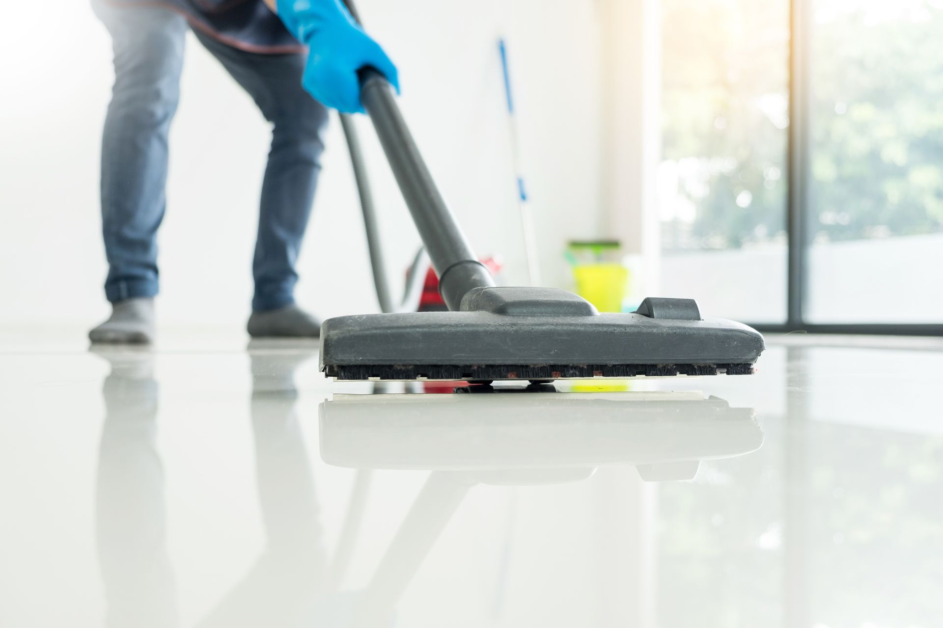 Person vacuums a shiny white floor, wearing blue gloves, in a bright room. Person vacuums a shiny white floor, wearing blue gloves, in a bright room.