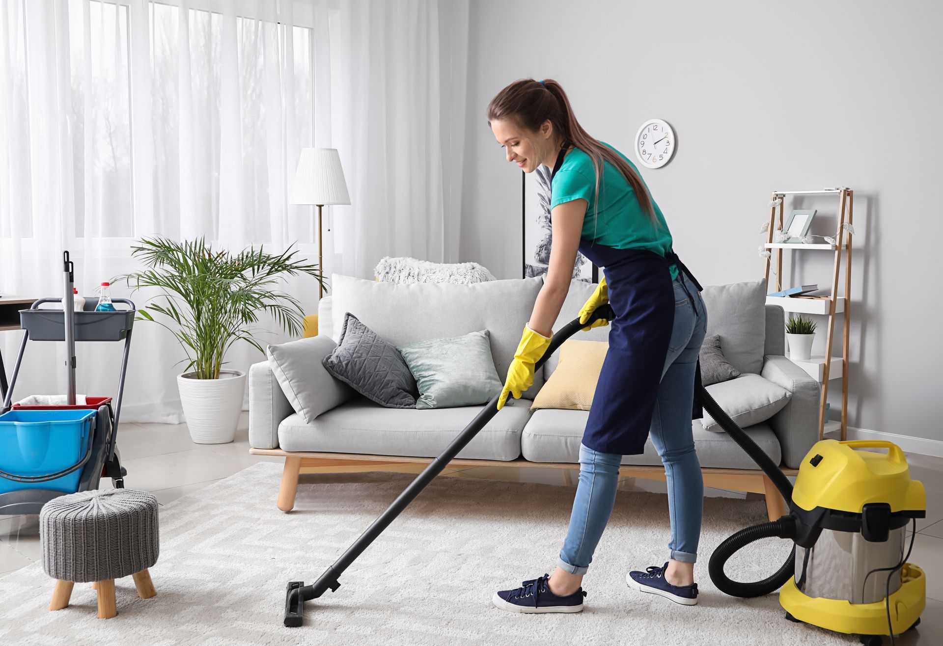 Woman vacuuming a light-colored rug in a living room; wearing an apron and gloves. Woman vacuuming a light-colored rug in a living room; wearing an apron and gloves.
