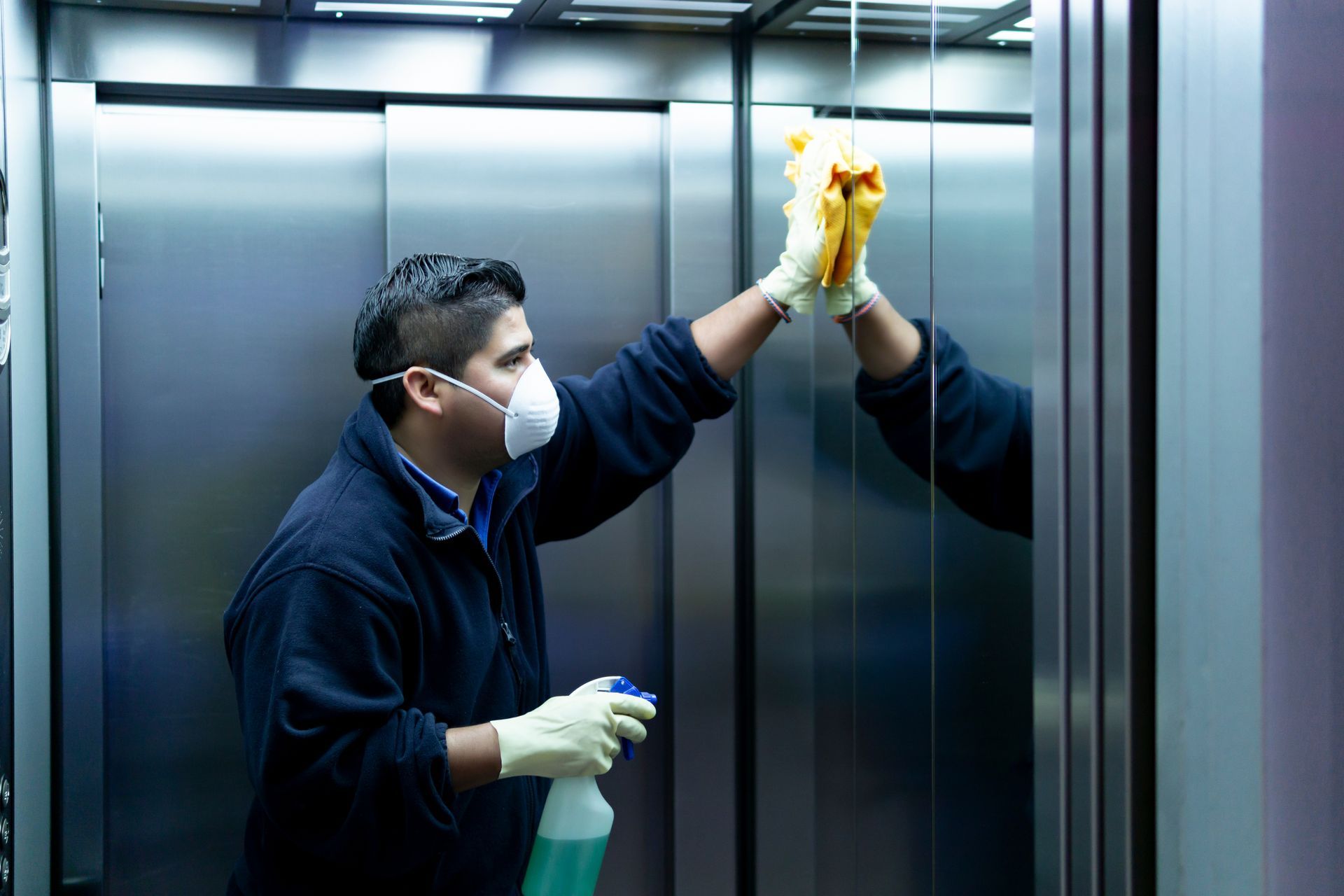 Person wearing mask cleans mirror in elevator.