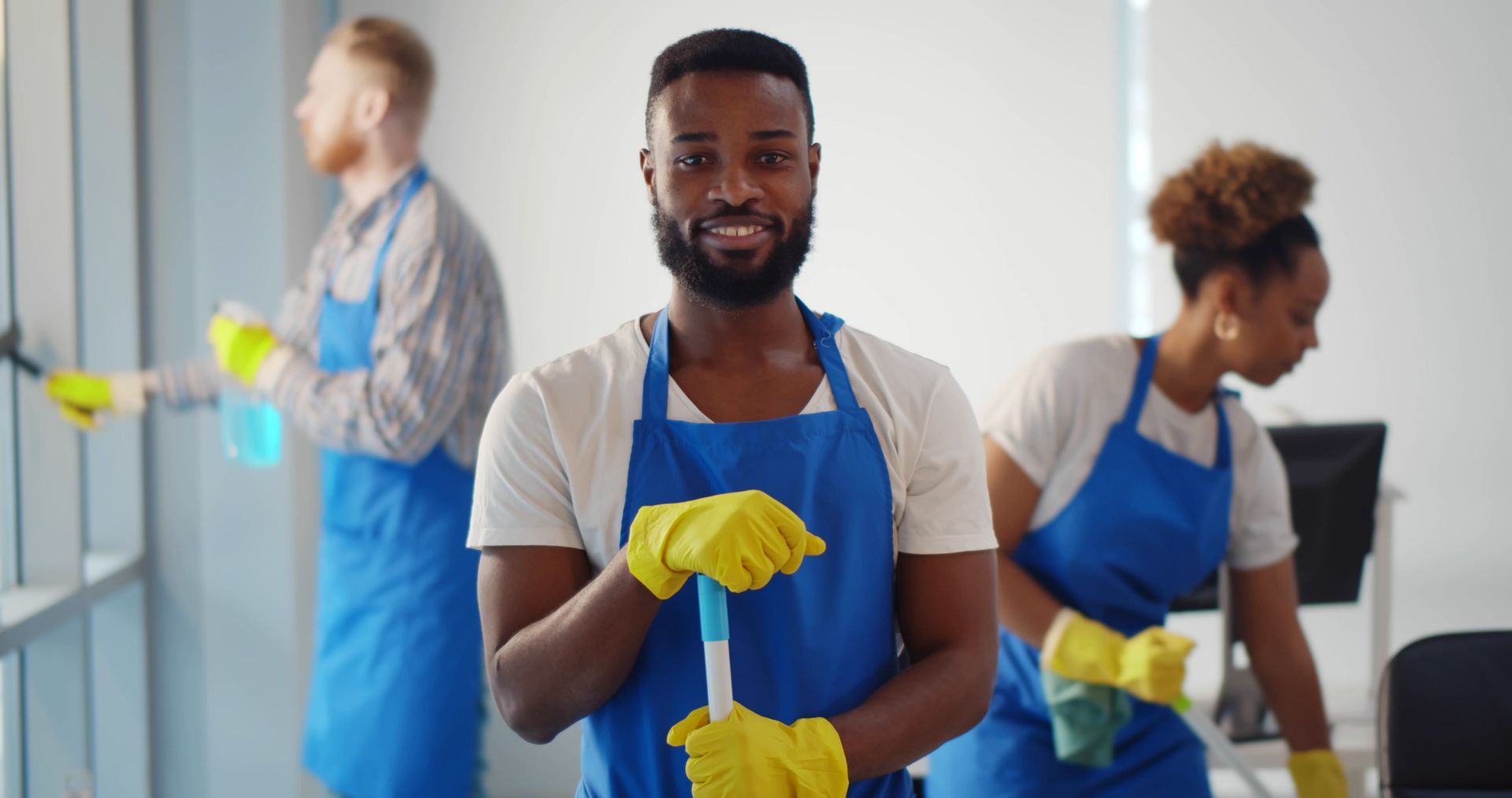 Janitors cleaning an office hallway; one spraying a window, another vacuuming, a third cleaning. Janitors cleaning an office hallway; one spraying a window, another vacuuming, a third cleaning.