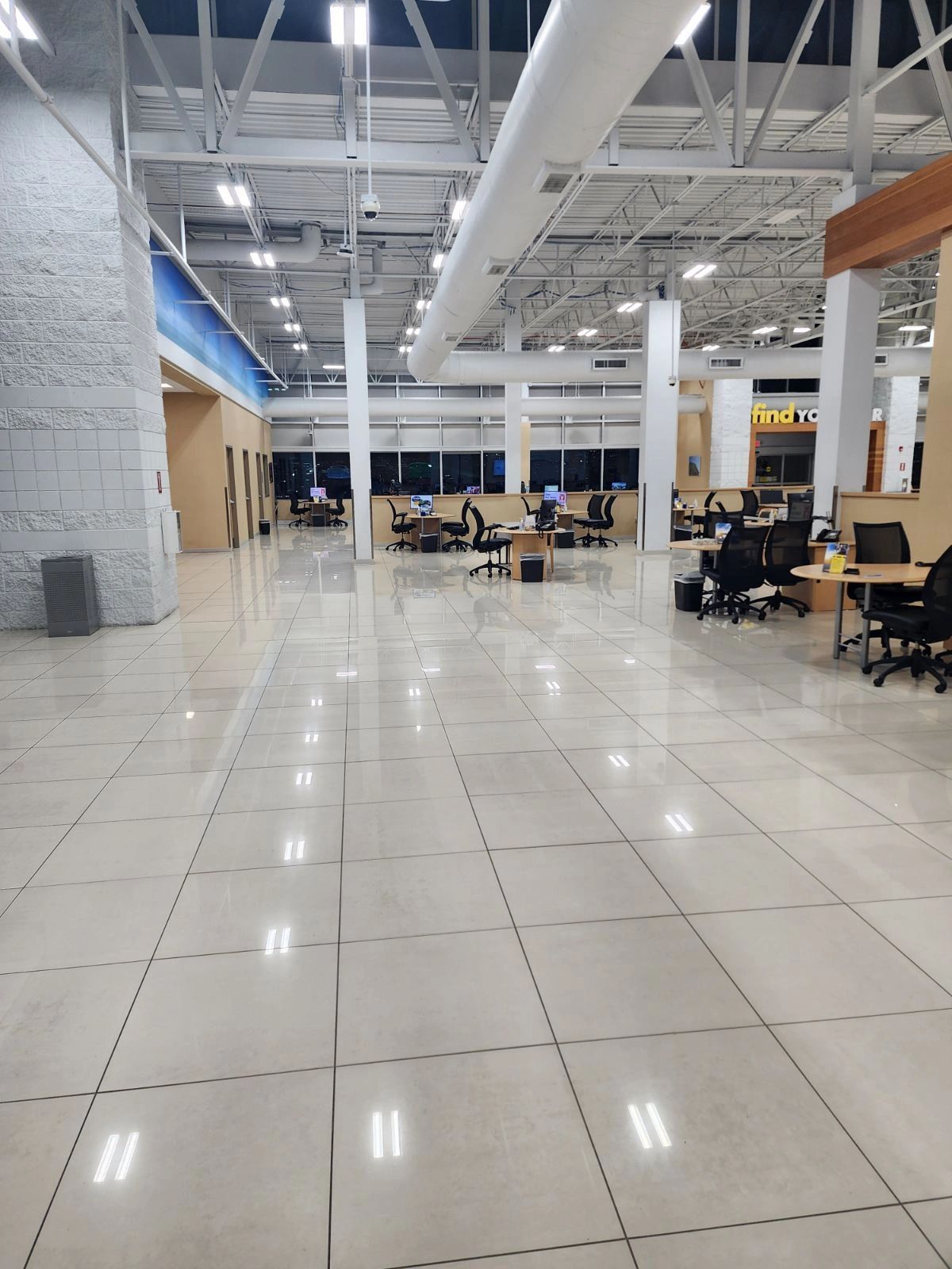 Large empty office with white tiled floor, desks, and overhead lighting.